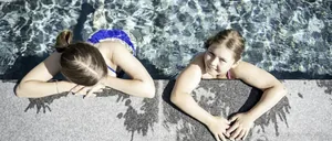 Zwei Mädchen lehnen am Rand eines Pools, umgeben von klarem Wasser im Das Mühlwald Quality Time Family Resort