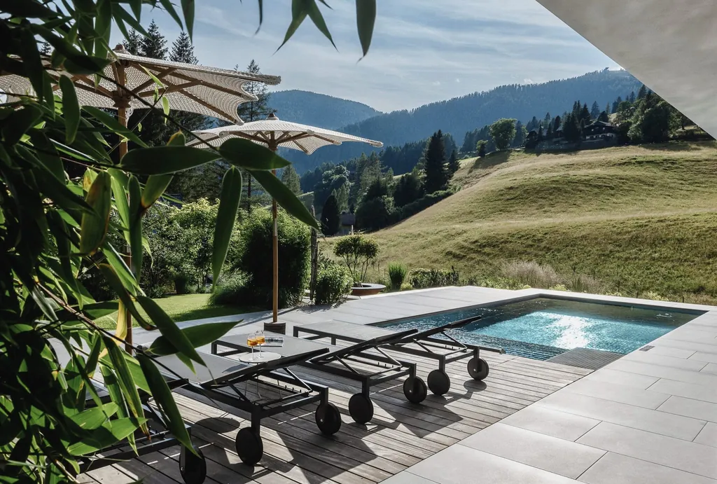 Outdoorpool des Chalet Falk auf der Terrasse mit Sonnenschirmen und -liegen und Blick auf die Almwiesen