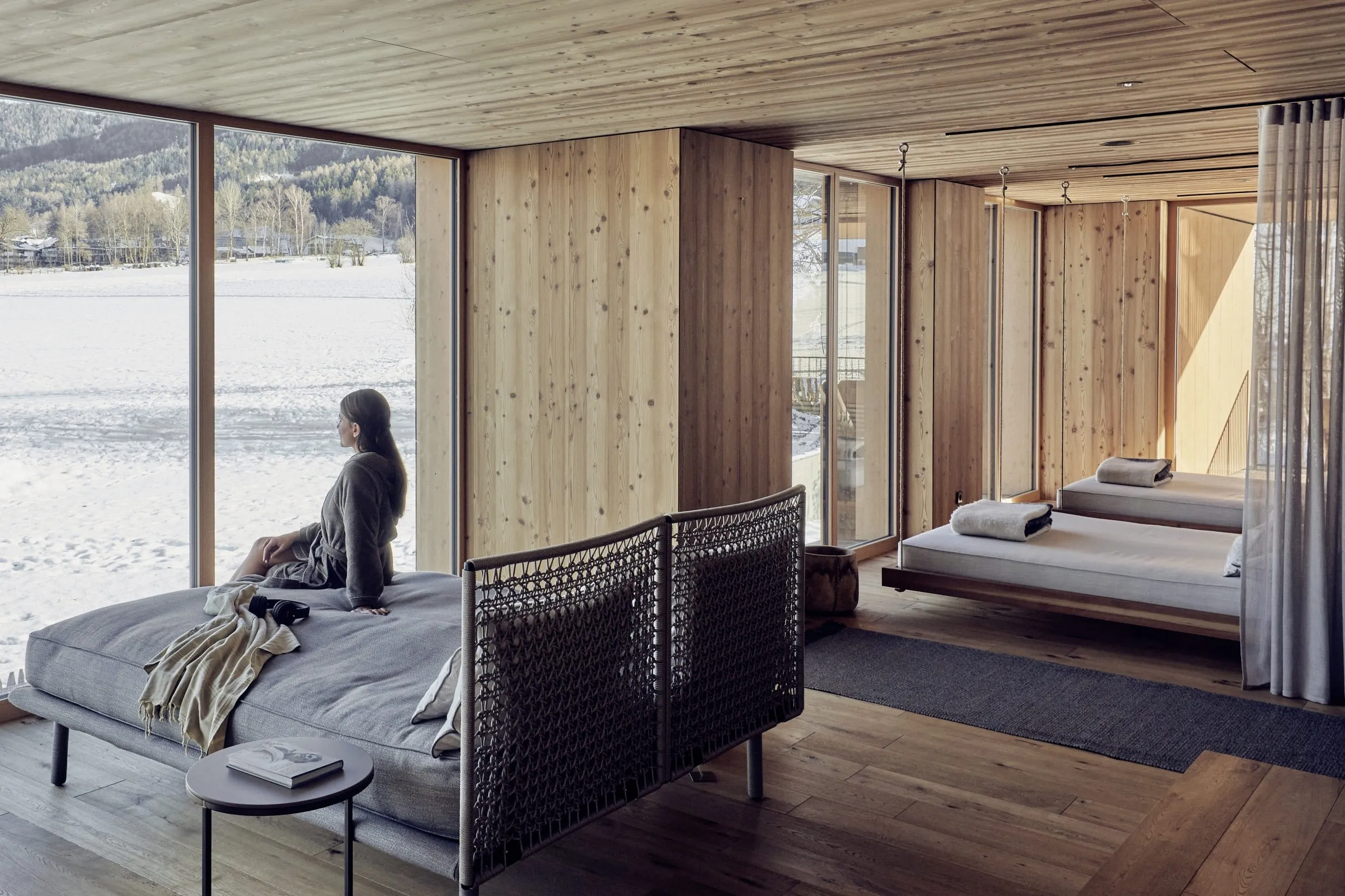 Frau auf Doppel-Ruheliege im Ruheraum des Falkensteiner Hotel Kronplatz schaut auf die verschneite Landschaft