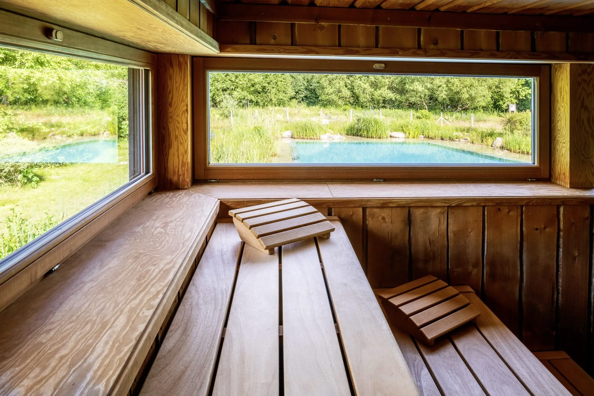 Blick von der Sauna des BEECH Resort Plauer See auf den t&uuml;rkisfarbenen Au&szlig;enpool am Garten