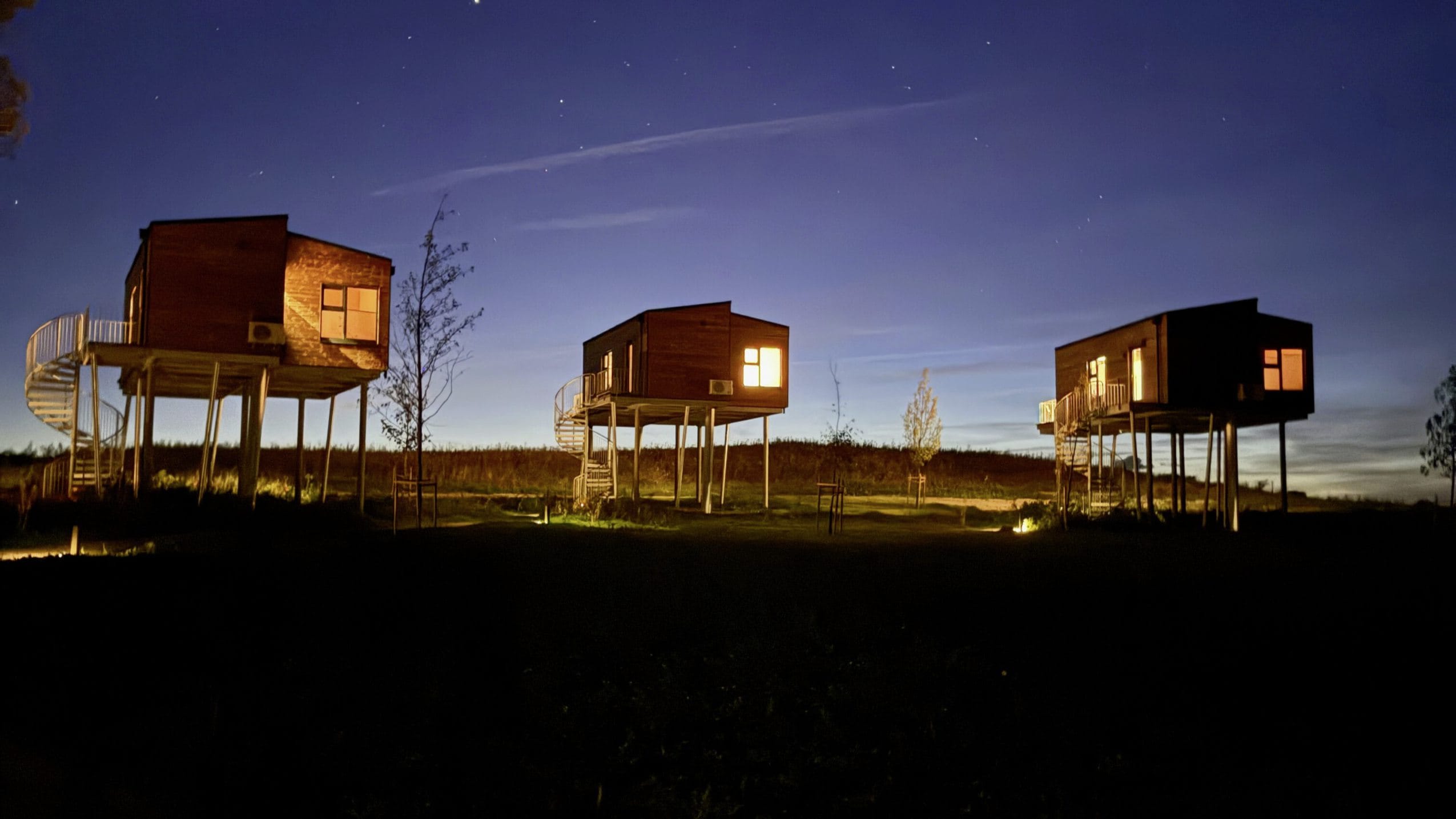 Holzhäuser auf Stelzen des Ostsee Baumhaushotel am Abend vor Sternenhimmel
