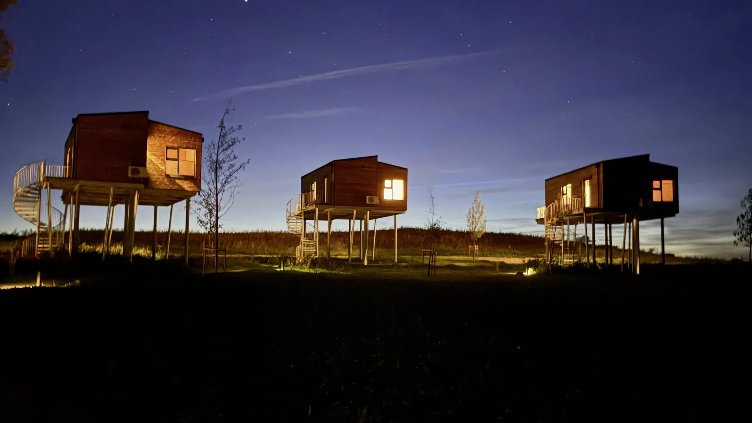Holzhäuser auf Stelzen des Ostsee Baumhaushotel am Abend vor Sternenhimmel