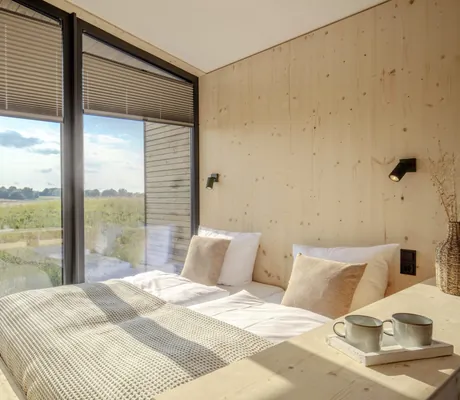 Doppelbett vor großem Panoramafenster mit Blick auf die Wiesen rund um das Ostsee Baumhaushotel