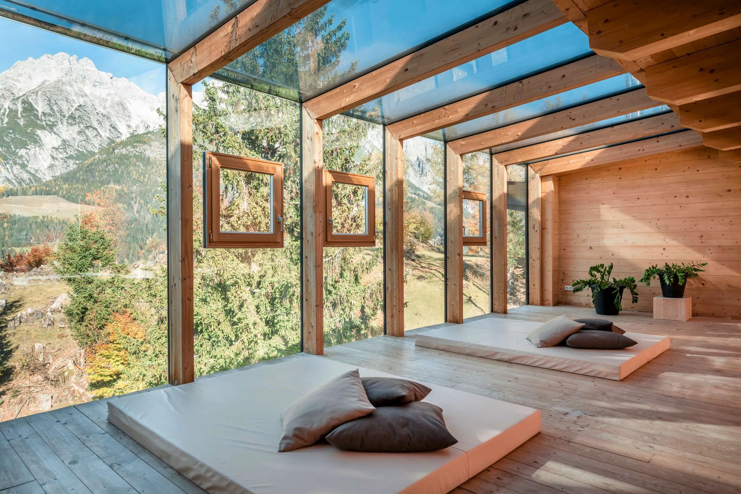 Raum im Holzhotel Forsthofalm mit gro&szlig;er Fensterfront und zwei Matratzen auf denen Kissen liegen