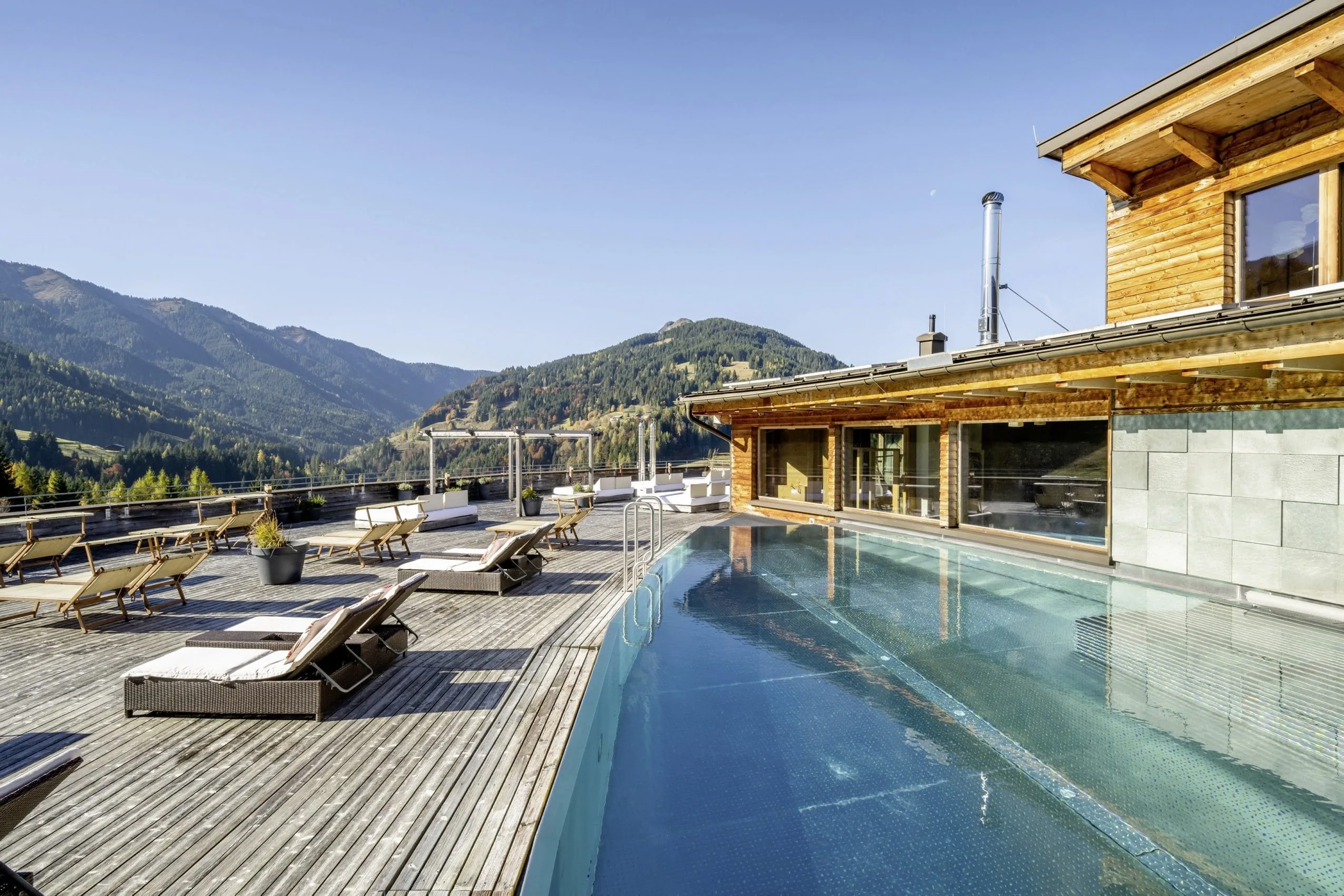 Rooftop-Pool des Holzhotel Forsthofalm mit Sonnenliegen und Bergen im Hintergrund