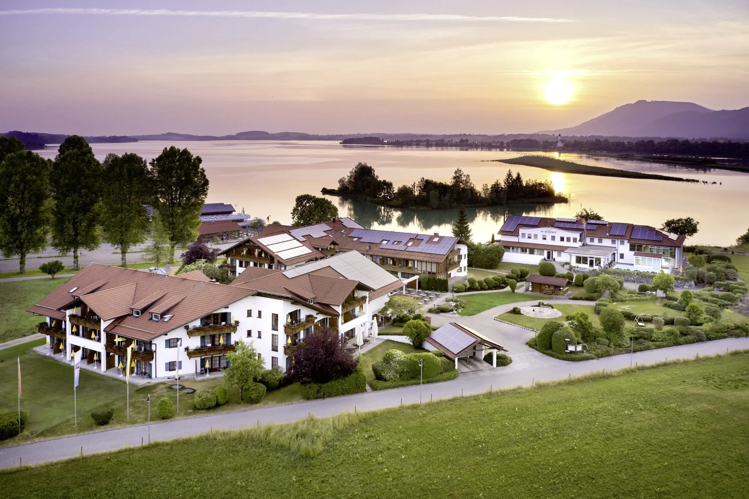Luftaufnahme des Hotel Sommer mit Forggensee im Hintergrund und rosa-orange untergehender Sonne