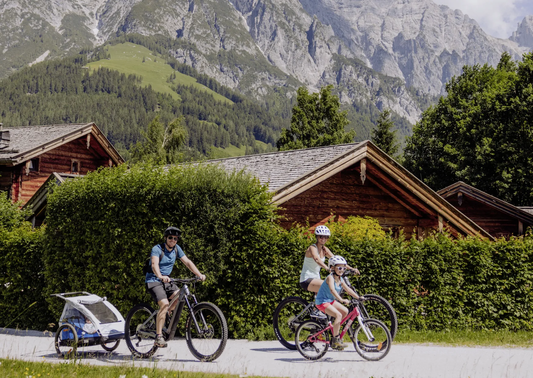 Familie f&auml;hrt Fahrrad auf dem Gel&auml;nde des Naturresort PURADIES mit Bergen im Hintergrund