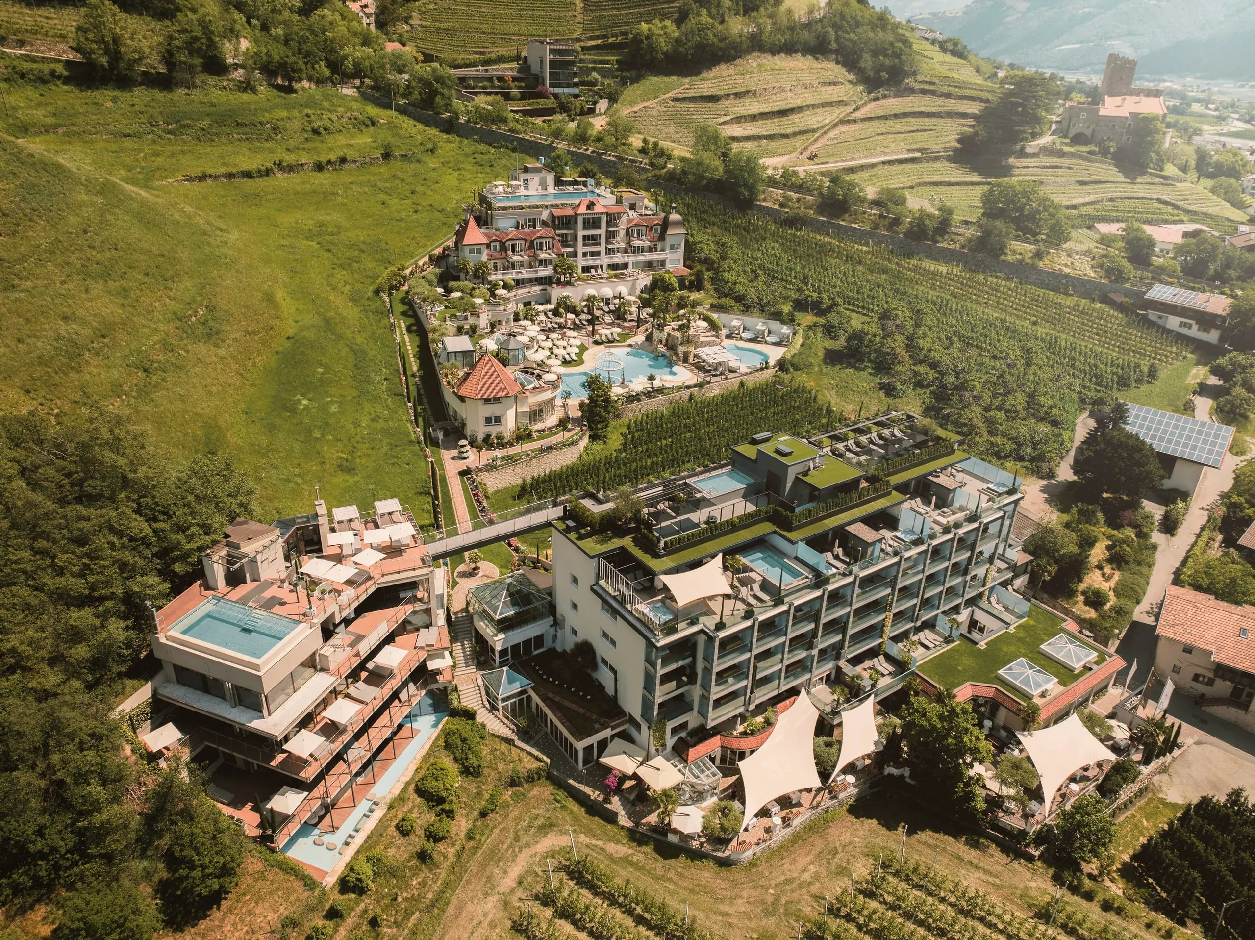 Blick von oben aus der Luft auf das Preidlhof Luxury DolceVita Resort in Naturns mit mehreren Geb&auml;uden und Pools