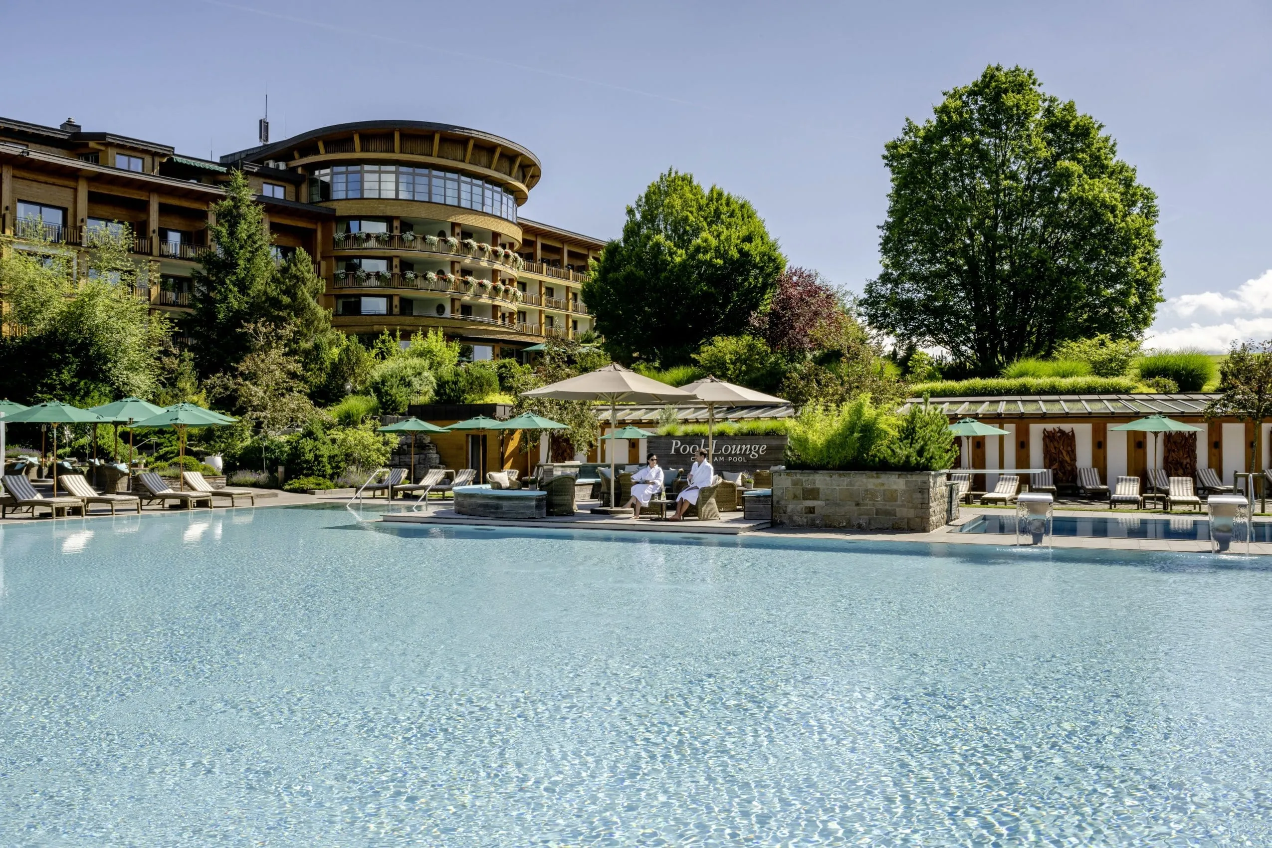 Paar in Badem&auml;nteln sitzt bei strahlendem Sonnenschein am Outdoorpool des Sonnenalp Resorts