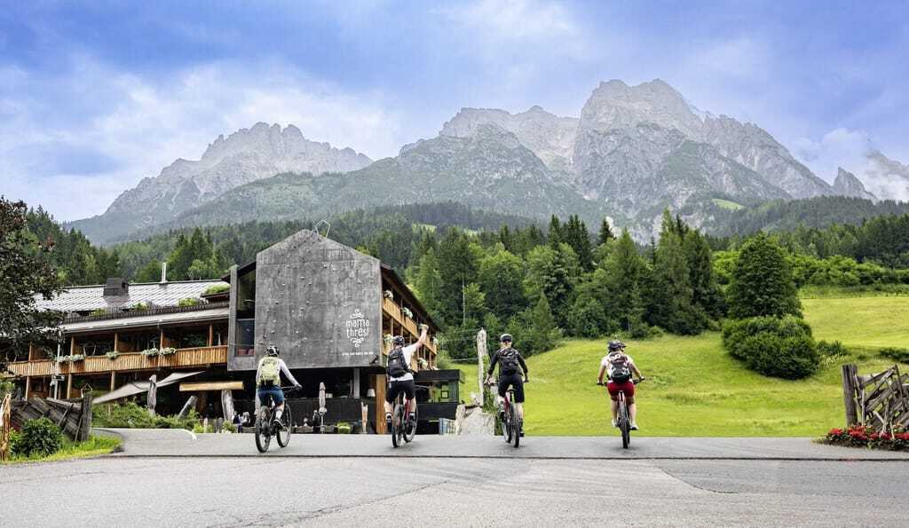 Außenansicht des mama thresl, Berge im Hintergrund, vier Fahrradfahrer im Vordergrund