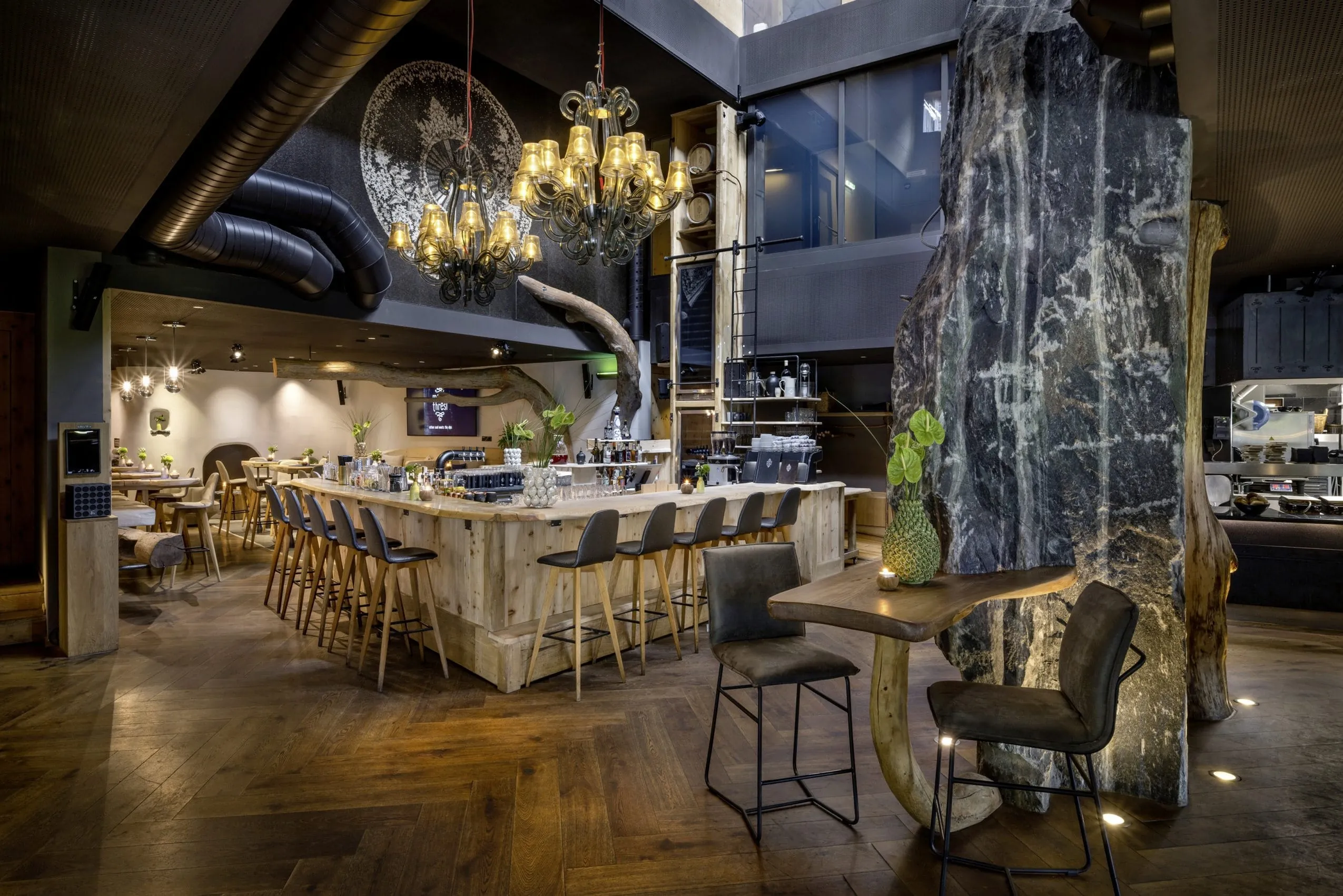 Moderne Bar aus Holz mit Kronleuchtern und dunkelgrauen Barhockern im mama thresl