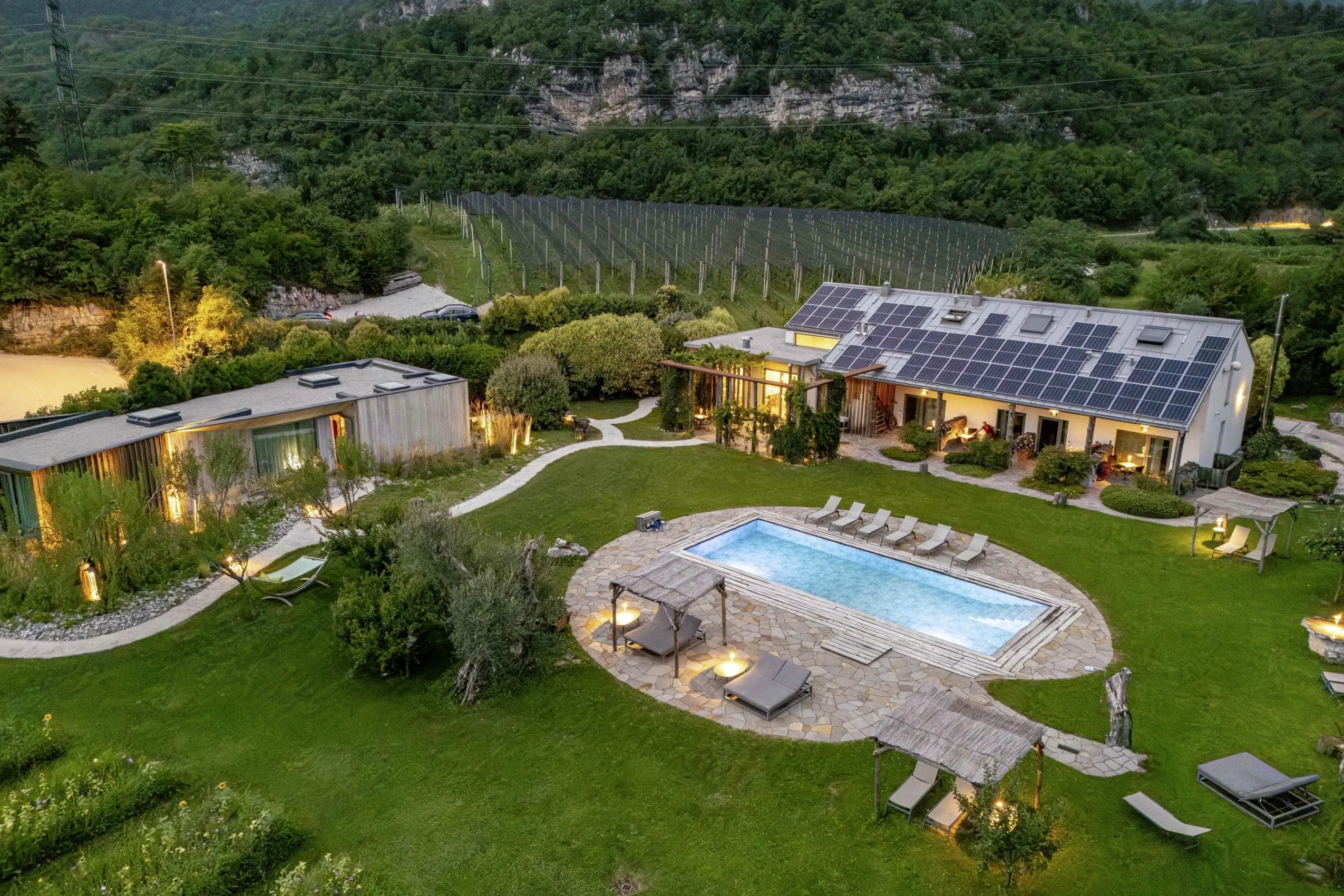 Luftaufnahme des Agritur La Dolce Mela mit Bioschwimmbad, Garten und Apfelplantagen vor Bergkulisse