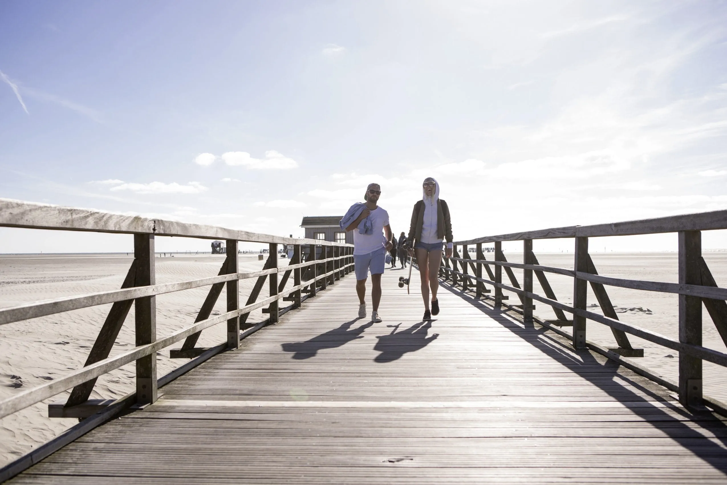 Zwei junge Menschen laufen in sommerlicher Kleidung &uuml;ber den Steg am Strand von St. Peter-Ording