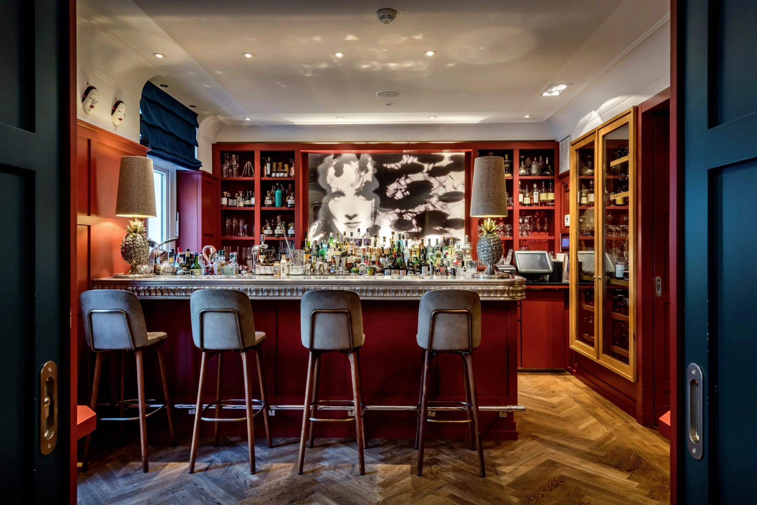 rot gestaltete Bar im LA MAISON mit grauen Barhockern und Schwarz-Wei&szlig;-Fotografie im Hintergrund