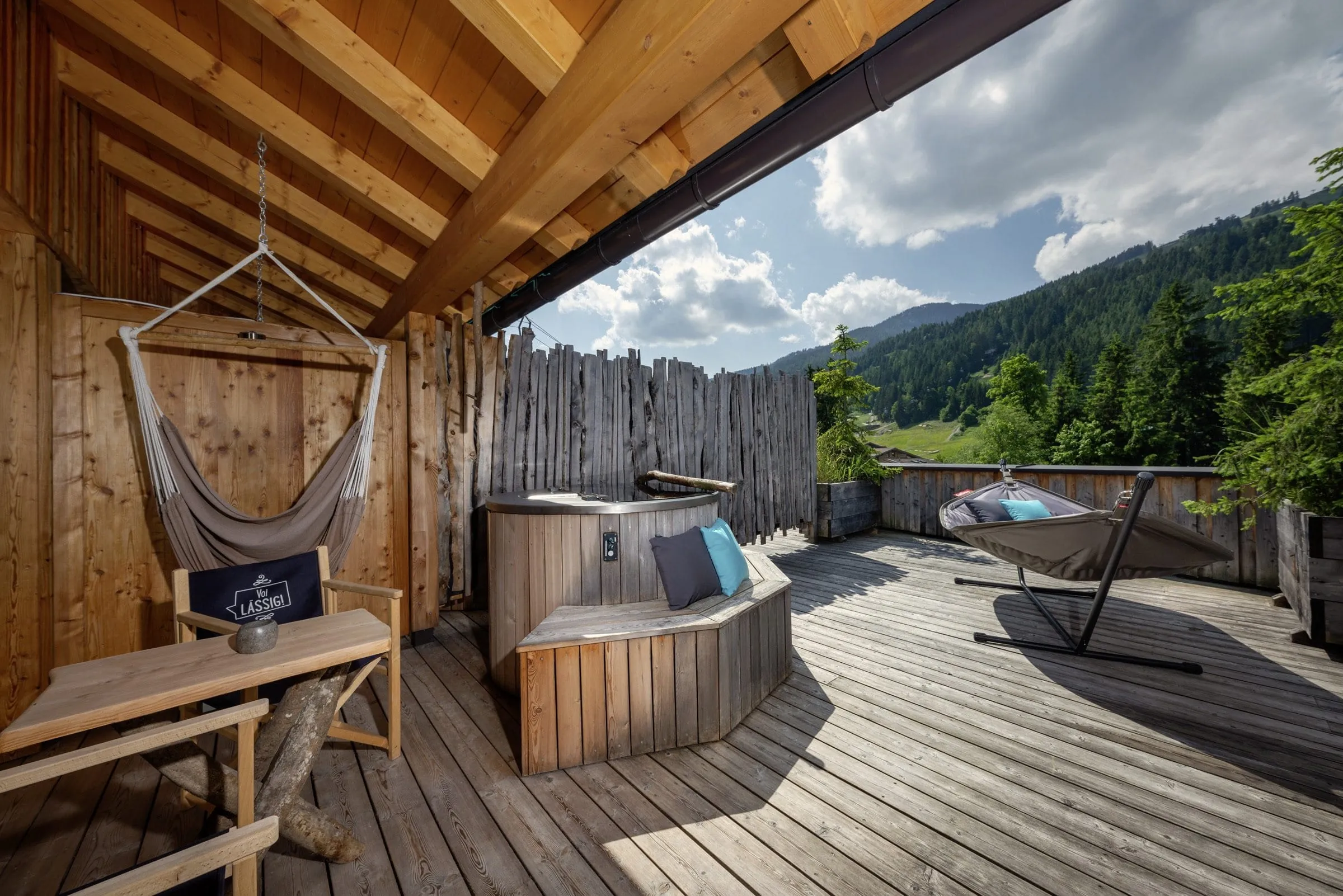 Holzterrasse mit H&auml;ngesessel, Hot Tub, Liege und Alpenblick bei sonnigem Bergwetter im mama thresl