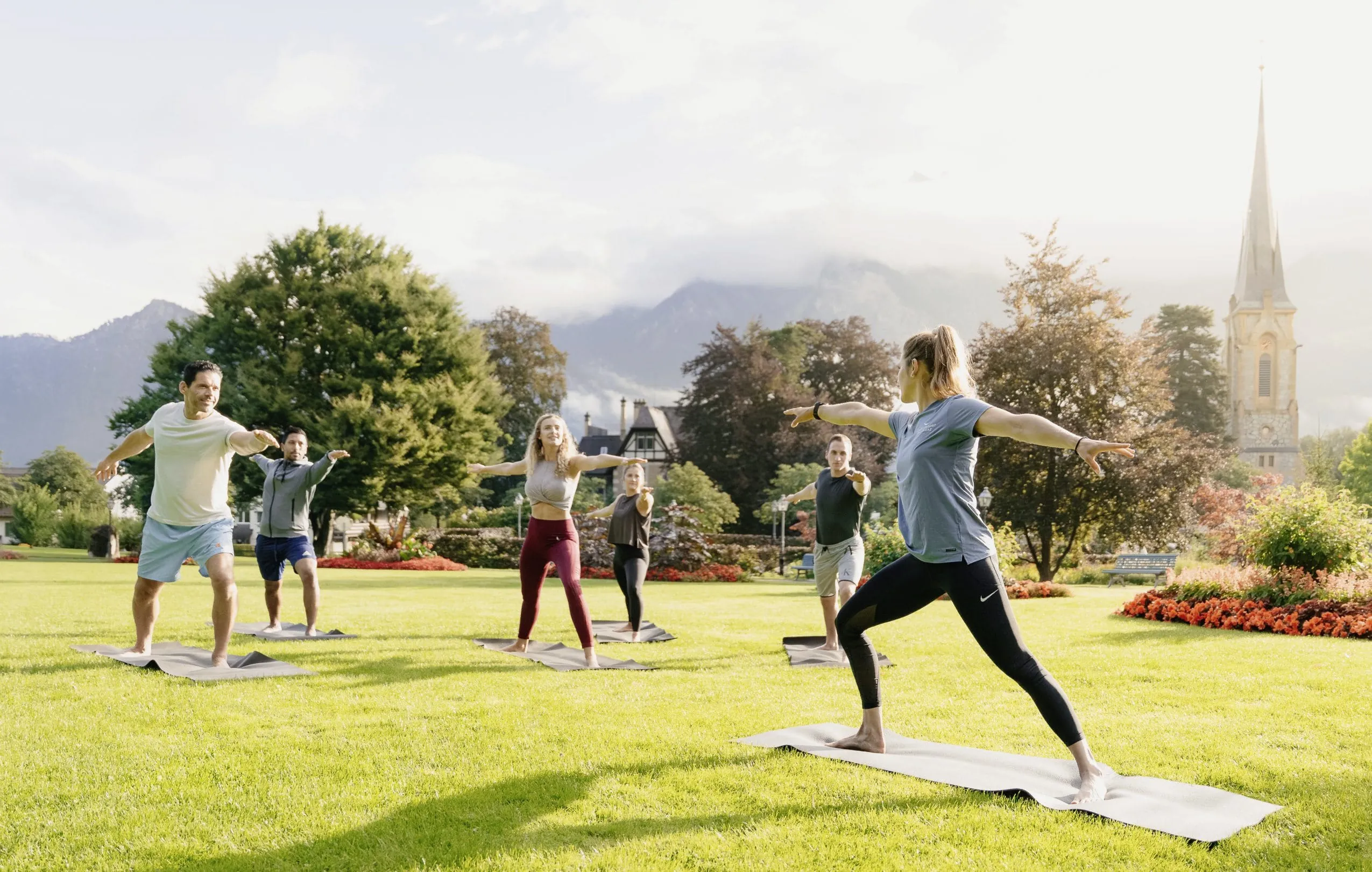 Gruppe beim Yoga auf einer gr&uuml;nen Wiese vor einer Kirche und Bergkulisse im Grand Resort Bad Ragaz