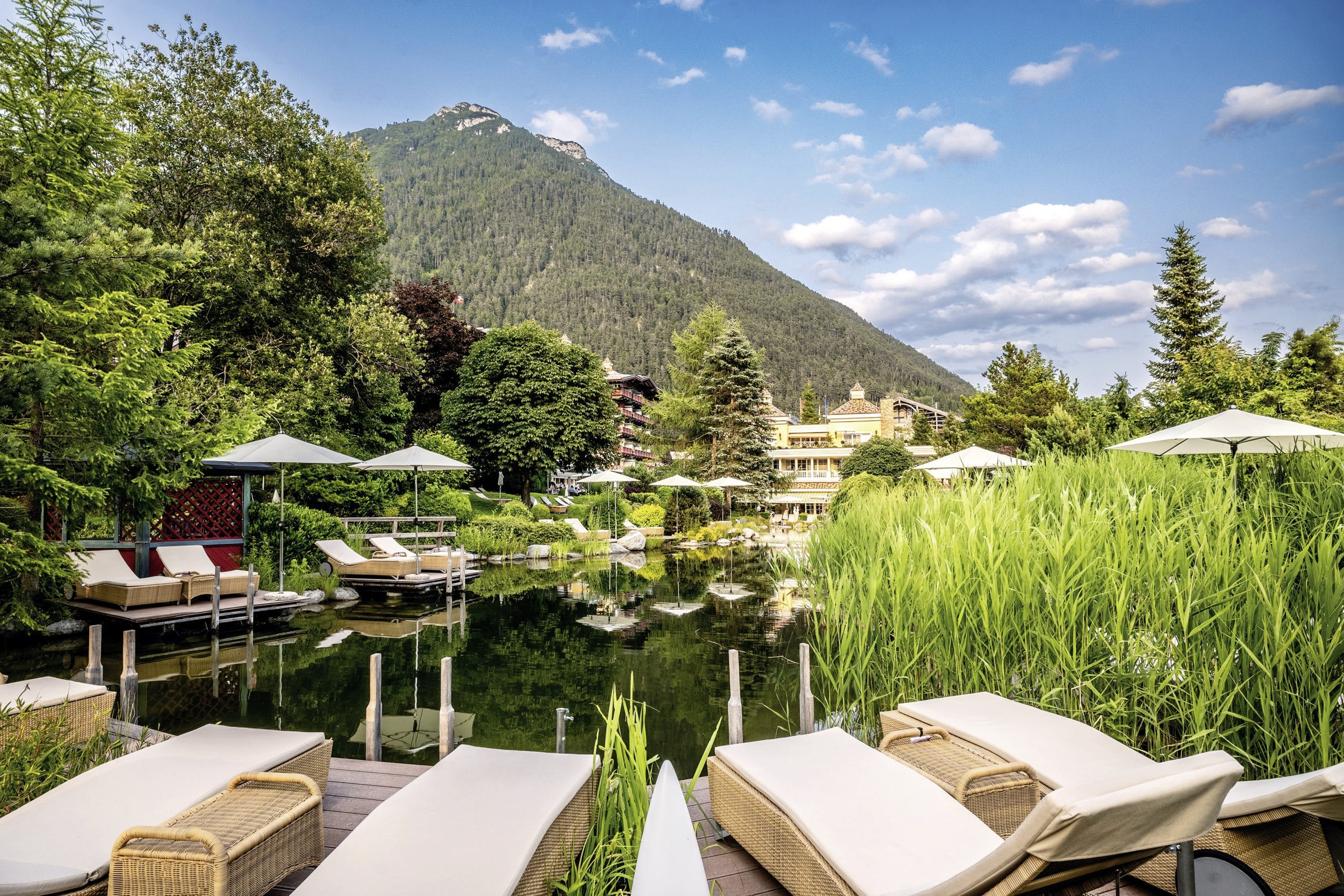 Badeteich mit gemütlichen Liegen, Sonnenschirmen und Blick auf die Wellnessresidenz Alpenrose