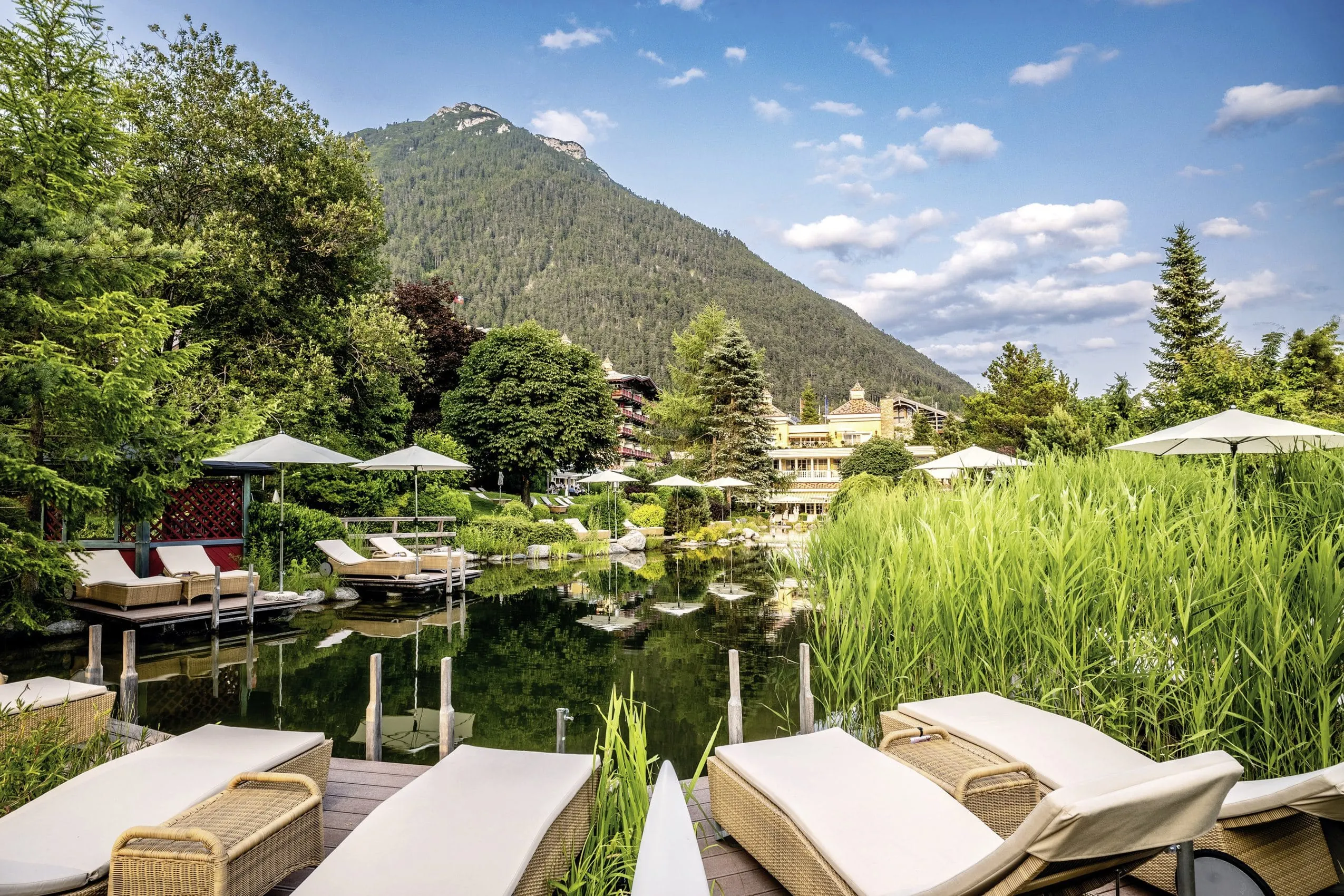 Badeteich mit gemütlichen Liegen, Sonnenschirmen und Blick auf die Wellnessresidenz Alpenrose