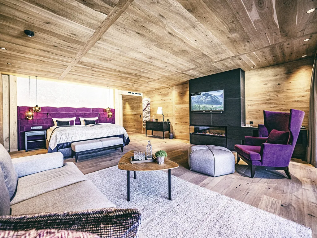 Luxuriöse Spa-Suite in der Wellnessresidenz Alpenrose mit Holzelementen, modernem Kamin, violettem Sessel und großem Bett