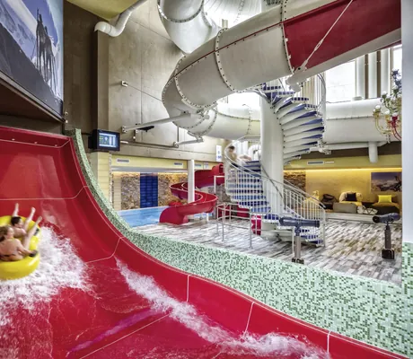 Indoor-Wasserwelt der Wellnessresidenz Alpenrose mit großer roten Rutsche, Spiralrutschen und spielenden Kindern
