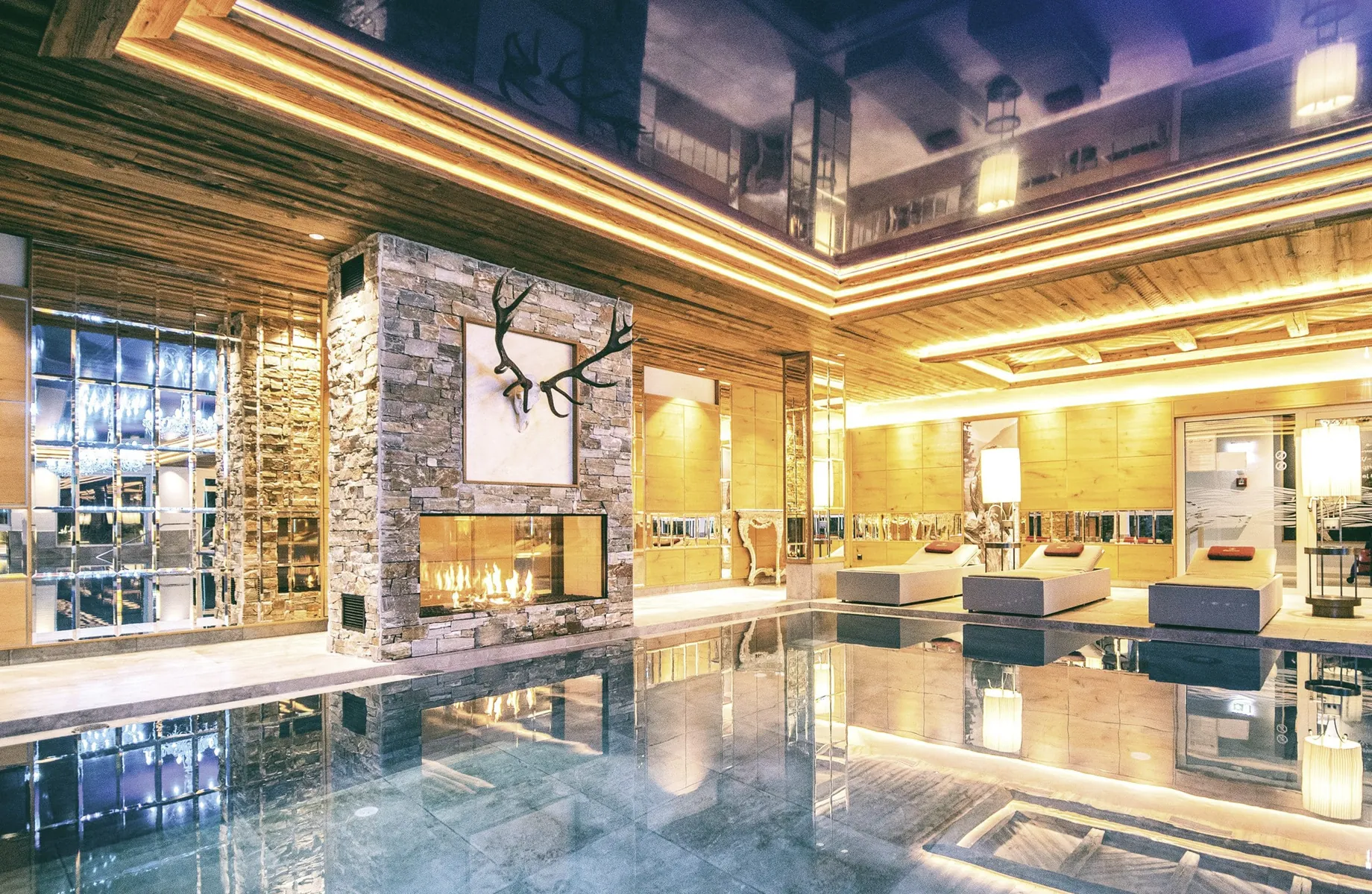 Stilvoller Indoorpool der Wellnessresidenz Alpenrose mit Steinwand, Kamin und Liegen im eleganten Wellnessbereich