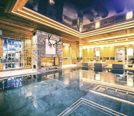 Stilvoller Indoorpool der Wellnessresidenz Alpenrose mit Steinwand, Kamin und Liegen im eleganten Wellnessbereich