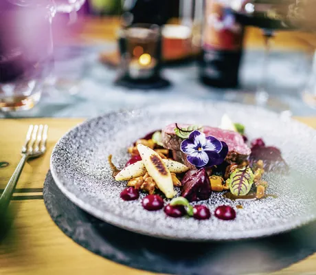Gourmetgericht mit Fleisch, Gemüse und essbaren Blüten auf einem kunstvoll angerichteten Teller in der Wellnessresidenz Alpenrose