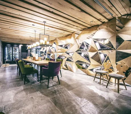 Moderne Sinneswerkstatt der Wellnessresidenz Alpenrose mit geometrischen Weindisplays, Holztisch und grün- und lilafarbenen Designerstühlen
