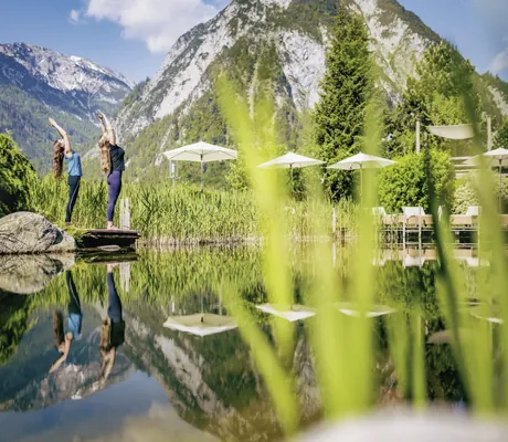 Zwei Frauen bei Yoga am Naturteich der Wellnessresidenz Alpenrose mit alpiner Bergkulisse im Hintergrund