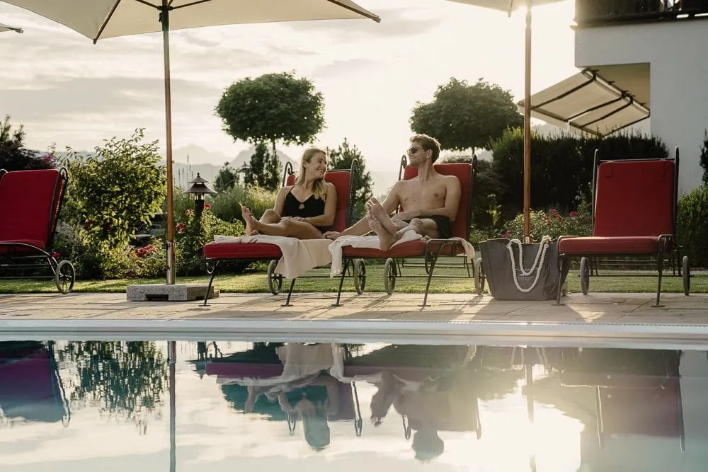 Paar liegt auf roten Liegest&uuml;hlen am Outdoorpool im Alpbacherhof