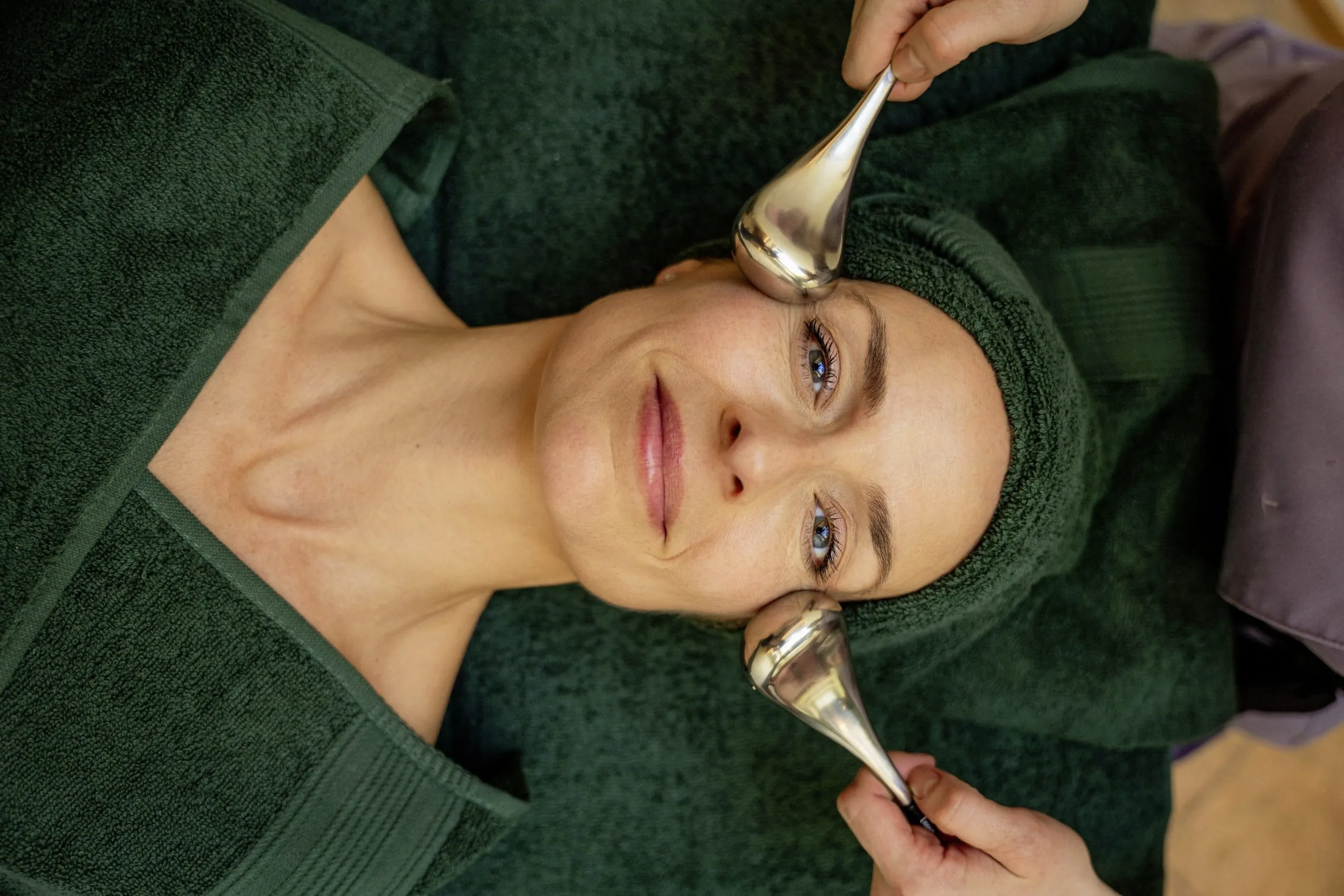 Frau mit dunkelgr&uuml;nem Frotteeturban erh&auml;lt im Hotel Allg&auml;u Sonne Gesichtsbehandlung mit Icerollern