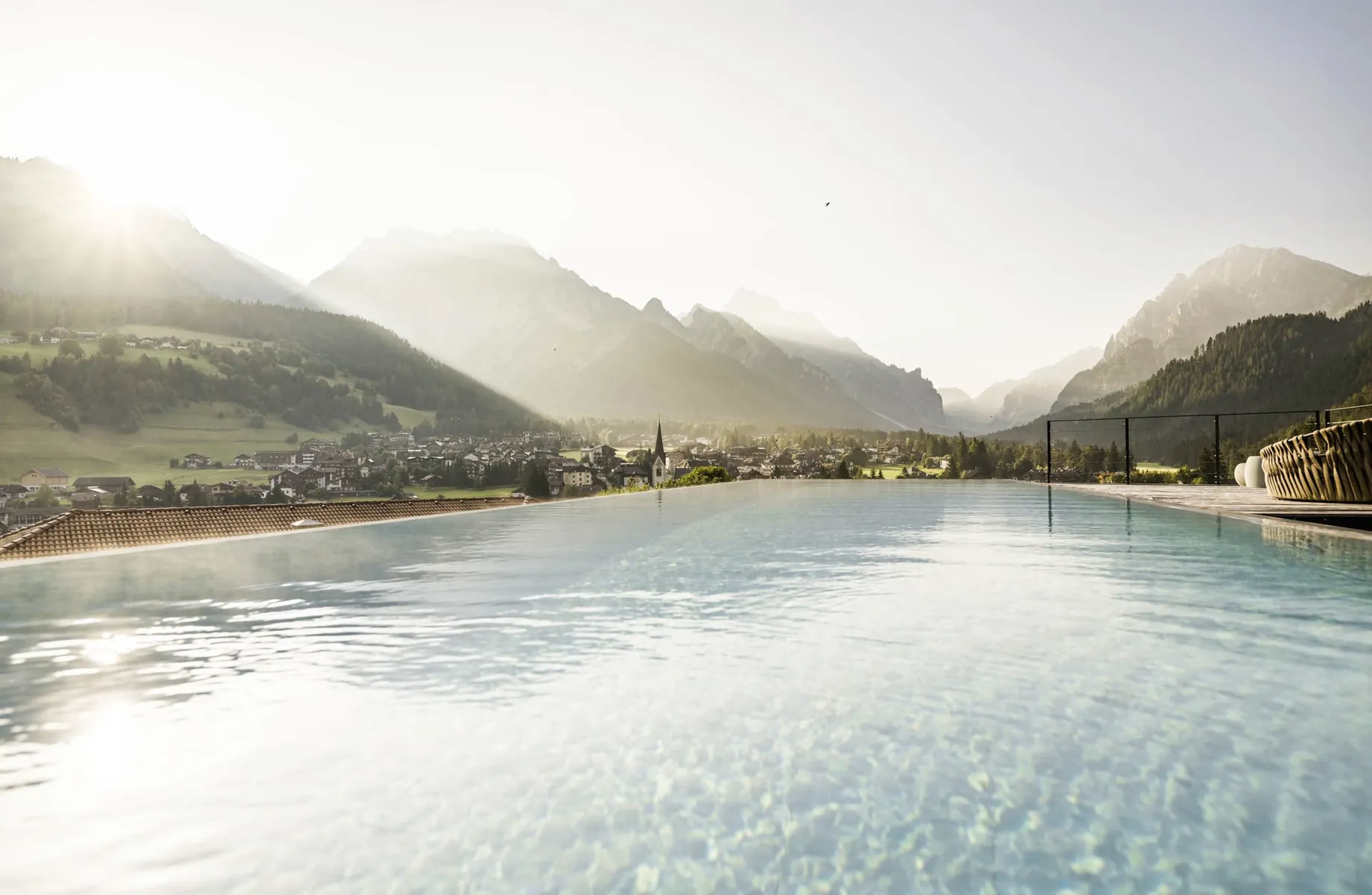 Outdoor-Infinitypool des Excelsior Dolomites Life Resort mit Blick auf St. Vigil, umgeben von Bergen