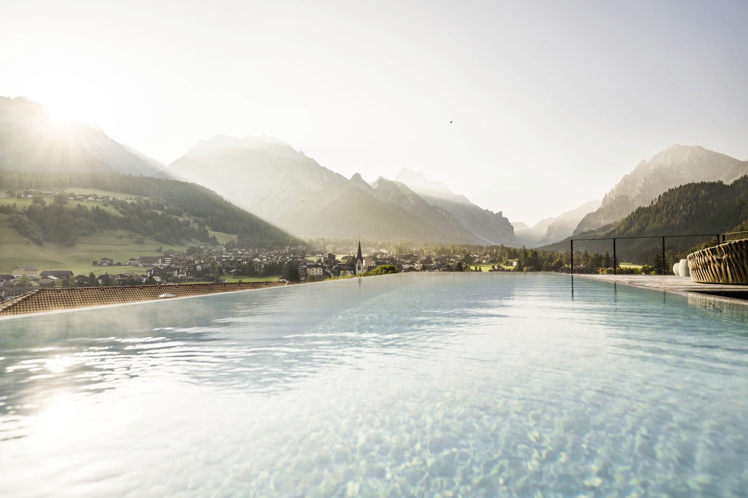 Outdoor-Infinitypool des Excelsior Dolomites Life Resort mit Blick auf St. Vigil, umgeben von Bergen