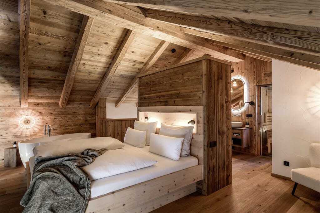 Doppelbett in einem der Alpzitt-Chalets mit Holzwänden, freistehender Badewanne und stimmungsvoller Beleuchtung
