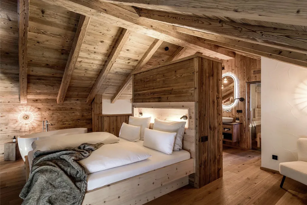 Doppelbett in einem der Alpzitt-Chalets mit Holzwänden, freistehender Badewanne und stimmungsvoller Beleuchtung