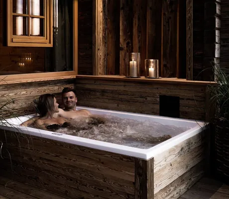 Außen-Whirlwanne eines Alpzitt-Chalets mit Kerzen und Pflanzen, zwei Personen im Wasser in entspannter Atmosphäre