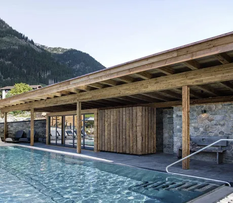 Outdoorpool der Alpzitt-Chalets mit Holz- und Steinverkleidung, Liegestühle und Bergblick im Hintergrund