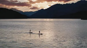Zwei Personen beim Stand-Up-Paddling auf dem Millstätter See bei Sonnenuntergang, Berge im Hintergrund in der Nähe des Chalet Falk | luxury mountain hideaway