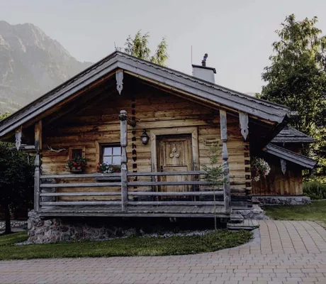Holzchalet mit Veranda im Naturresort PURADIES, umgeben von grüner Landschaft und Bergen im Hintergrund