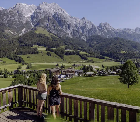 Zwei Frauen blicken von einer Terrasse des Naturresort PURADIES auf die umliegende Landschaft und die Berge