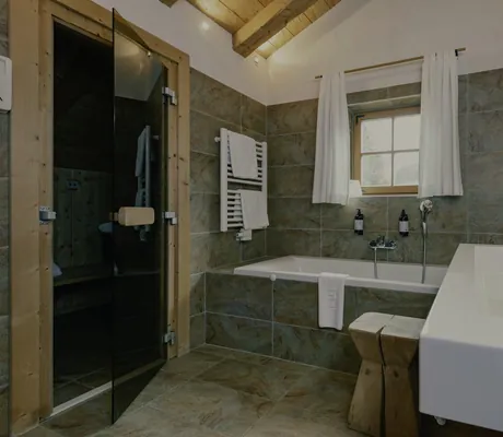 Elegantes Badezimmer im Naturresort PURADIES mit Badewanne, Sauna, Holzdecke und Natursteinfliesen