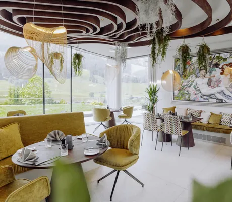 Hauben-Restaurant Ess:enz im Naturresort PURADIES mit kunstvoller Holzdecke, hängenden Pflanzen, großen Panoramafenstern und einem farbenfrohen Gemälde an der Wand