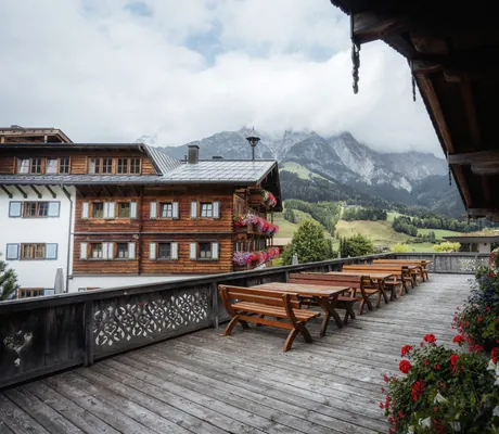 Holzterrasse des Naturresorts PURADIES mit Holz-Sitzbänken, Blumenschmuck und Bergpanorama im Hintergrund