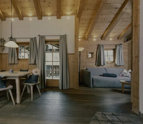 Wohn-/Essbereich im Chalet des Naturresort PURADIES mit Holztisch und -stühlen, grauem Sofa, Wandbild und Holzdecke