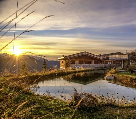 Blick auf das Chalet Stern auf dem Rosskopf bei Sonnenaufgang mit Naturbadeteich im Vordergrund