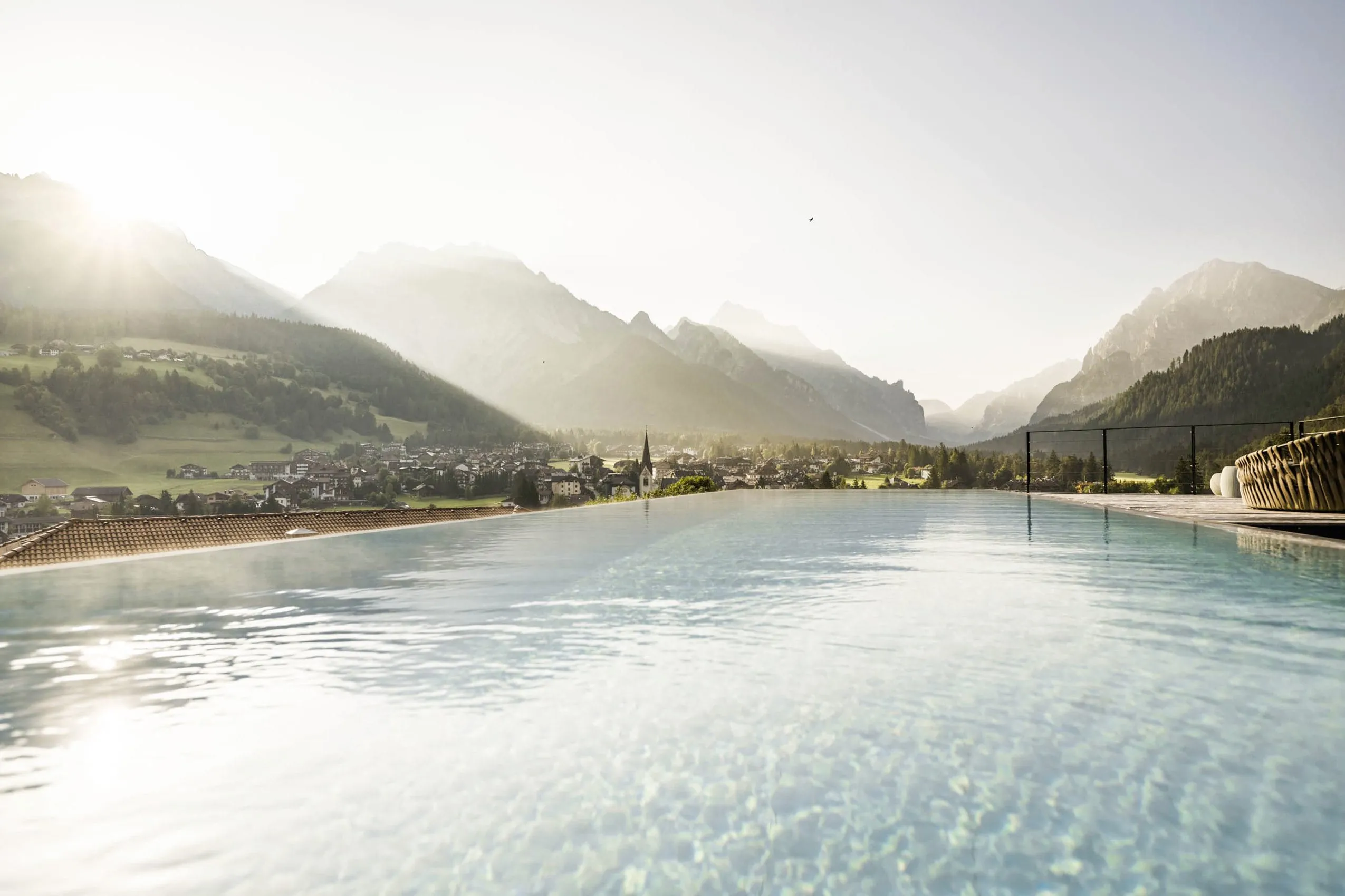 Outdoor-Infinitypool des Excelsior Dolomites Life Resort mit Blick auf St. Vigil, umgeben von Bergen