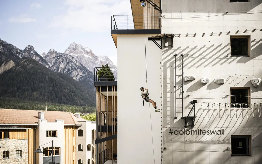 Mann hängt am Seil der Kletterwand des Excelsior Dolomites Life Resort