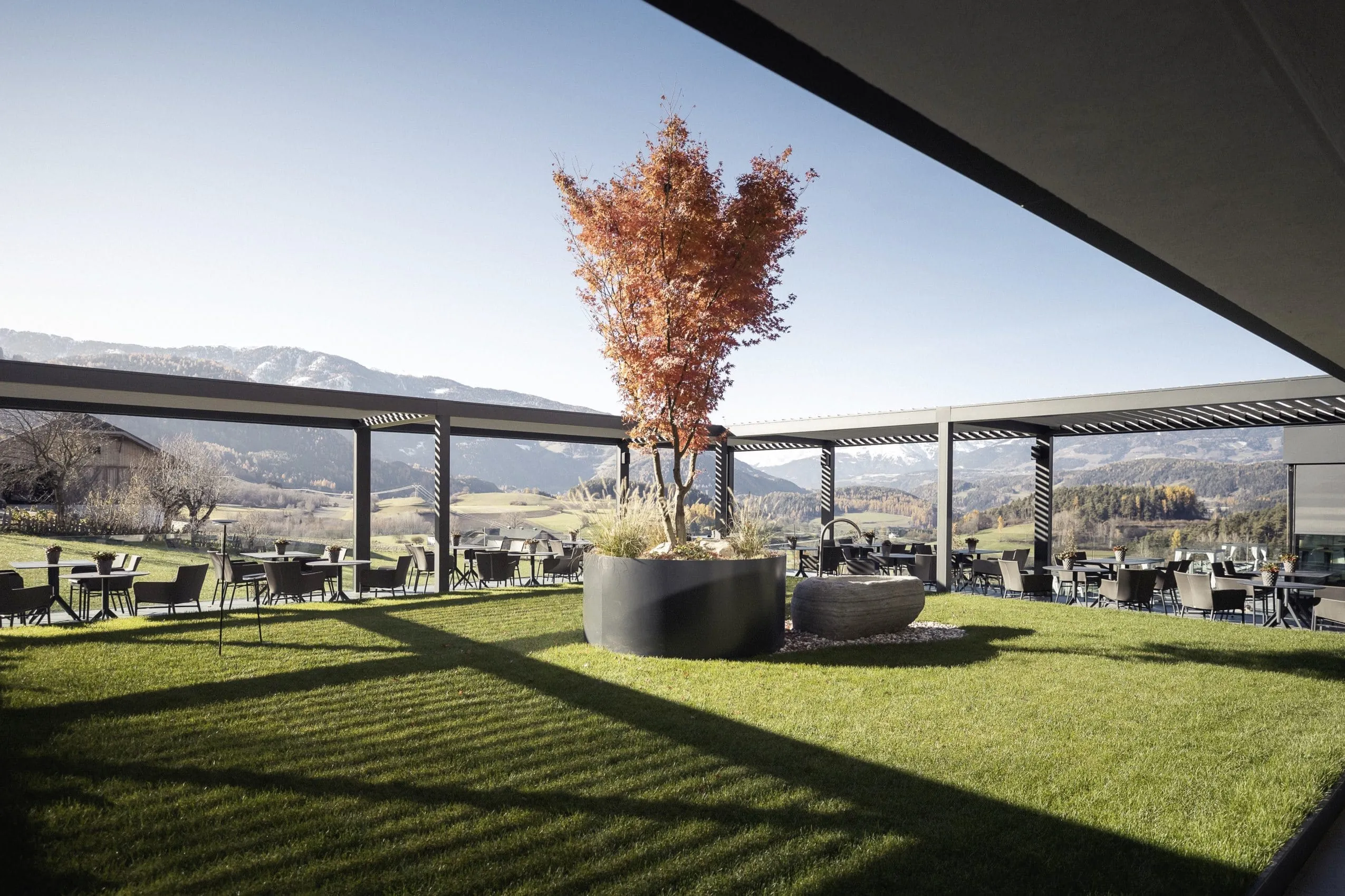 Gro&szlig;er Topf mit rot gef&auml;rbtem Laub steht auf der Wiese der Terrasse des Hotel Winkler
