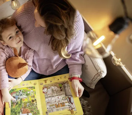 Frau liest mit einem Kind ein Bilderbuch in einer gemütlichen Leseecke des Familotel Elldus Resort