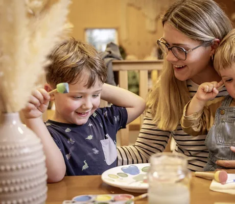 Kinder malen an einem Tisch mit Kinderbetreuerin im Familotel Elldus Resort, umgeben von Bastelutensilien und Farben